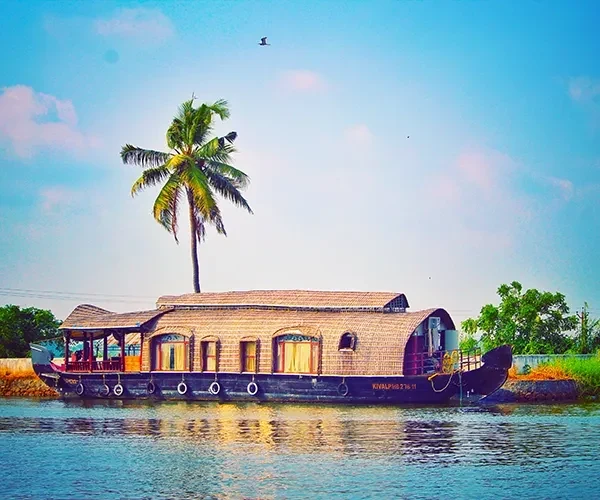 Traditional wooden kettuvallam houseboat floating along palm-fringed backwaters canal in Alleppey, Kerala